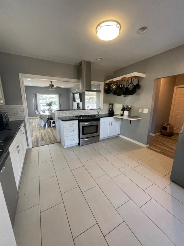 kitchen featuring backsplash, stainless steel appliances, island range hood, ceiling fan, and white cabinetry