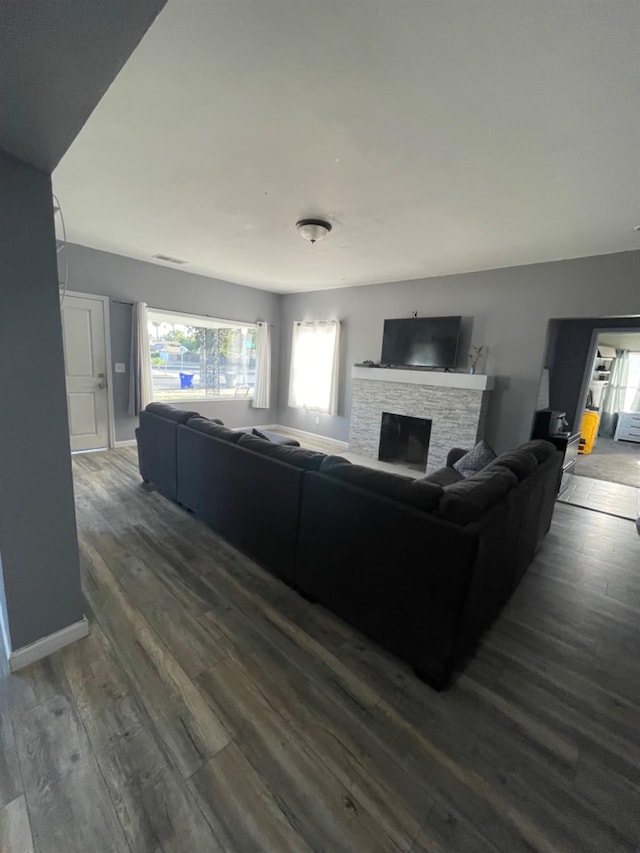 living room with a stone fireplace and dark wood-type flooring