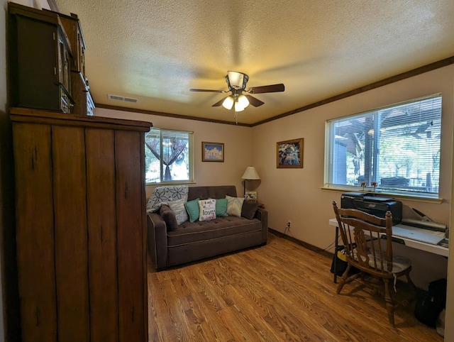 office area with a ceiling fan, visible vents, ornamental molding, light wood-style floors, and a textured ceiling