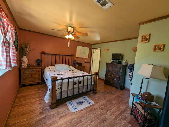 bedroom featuring crown molding, wood finished floors, visible vents, and ceiling fan