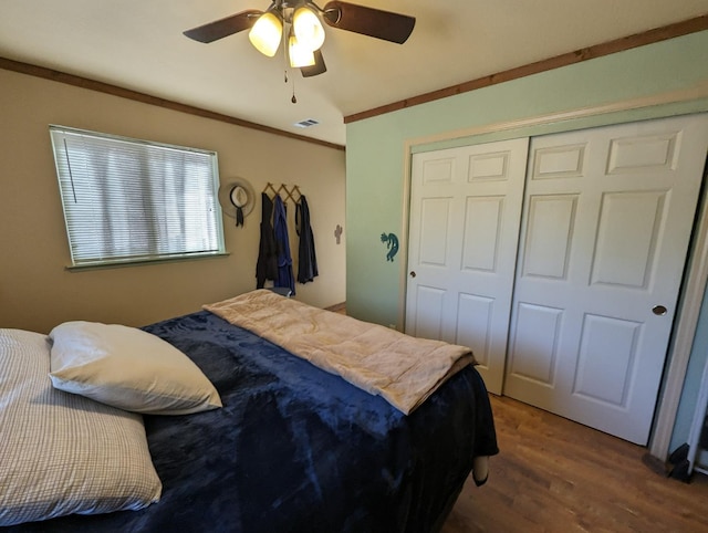 bedroom with wood finished floors, visible vents, ceiling fan, a closet, and crown molding