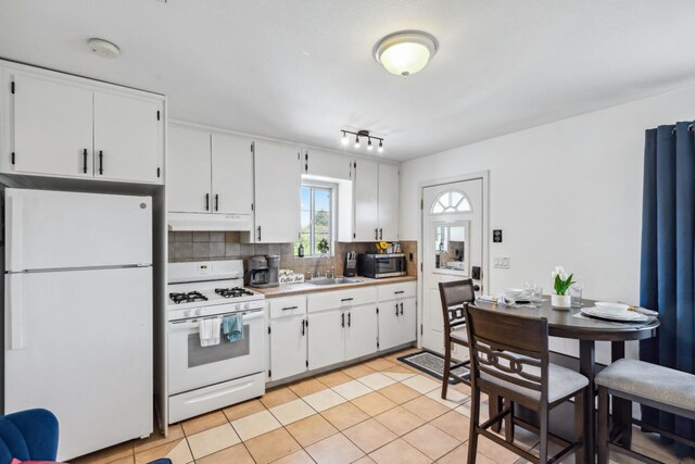 925 S Purdue Ave, Fresno, CA 93727 - kitchen with white appliances, under cabinet range hood, tasteful backsplash, white cabinetry, and light tile patterned flooring