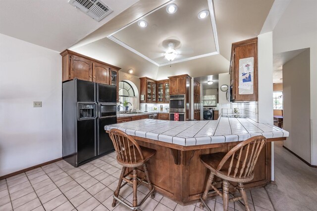 kitchen with a kitchen breakfast bar, kitchen peninsula, light tile patterned floors, tile countertops, and black appliances