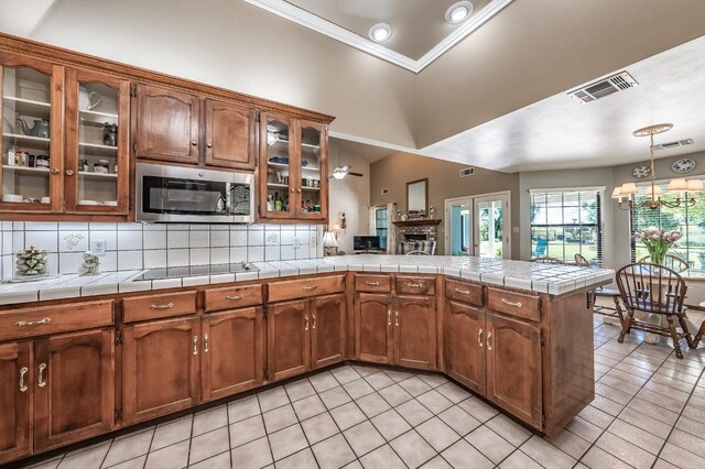 kitchen featuring light tile patterned flooring, ornamental molding, kitchen peninsula, tasteful backsplash, and tile counters