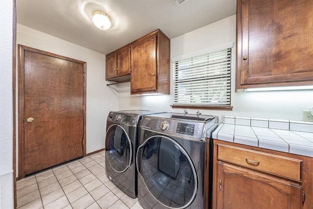 clothes washing area featuring light tile patterned floors, cabinets, and washer and dryer