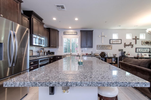 kitchen featuring backsplash, appliances with stainless steel finishes, dark brown cabinets, and a kitchen island