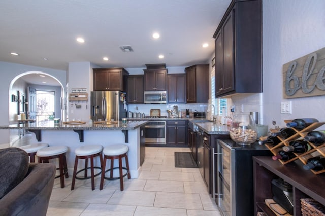 kitchen featuring stainless steel appliances, dark brown cabinetry, dark stone counters, and light tile floors