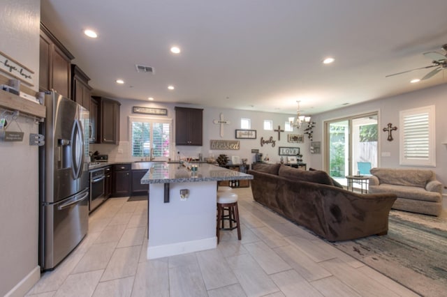 kitchen featuring ceiling fan with notable chandelier, stainless steel appliances, backsplash, a breakfast bar area, and a center island