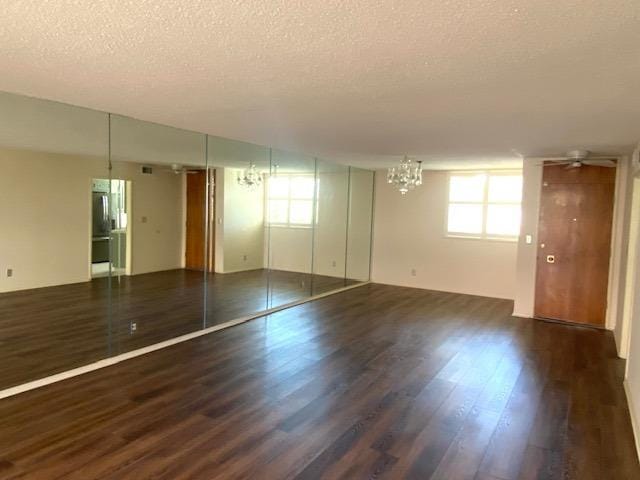 unfurnished room with dark wood-type flooring, a chandelier, and a textured ceiling