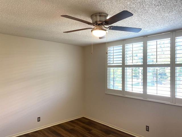 empty room featuring dark hardwood / wood-style floors, ceiling fan, a textured ceiling, and a wealth of natural light