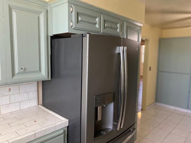 kitchen featuring tile counters, stainless steel fridge with ice dispenser, light tile floors, and tasteful backsplash