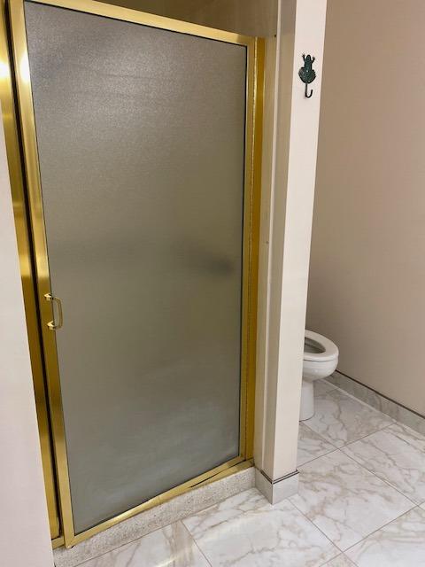 bathroom featuring tile flooring, a shower with shower door, and toilet