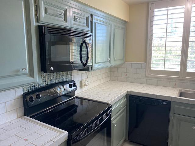 kitchen with backsplash, a wealth of natural light, black appliances, and tile counters