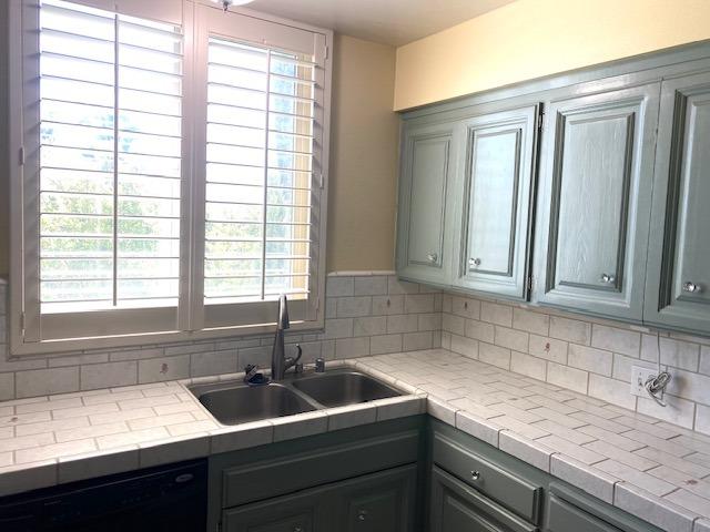 kitchen with black dishwasher, sink, tile countertops, and tasteful backsplash