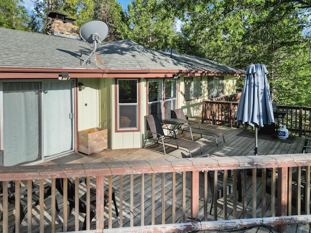 back of property with a shingled roof, a chimney, and a deck