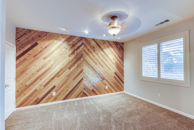 carpeted spare room with ceiling fan and wood walls