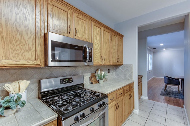 kitchen with light tile patterned floors, decorative backsplash, tile countertops, and appliances with stainless steel finishes