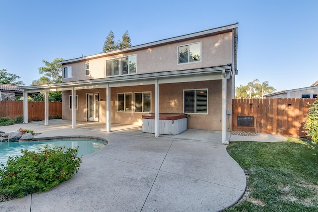 back of property with a hot tub and a patio