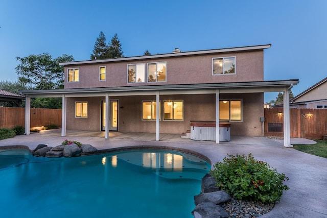 back house at dusk featuring a swimming pool with hot tub and a patio