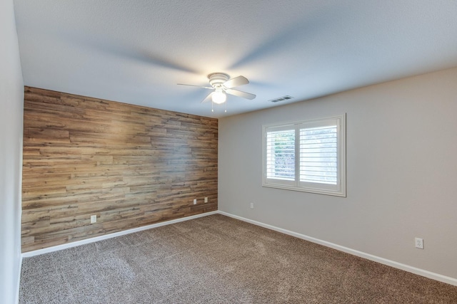 empty room with ceiling fan, a textured ceiling, carpet, and wood walls