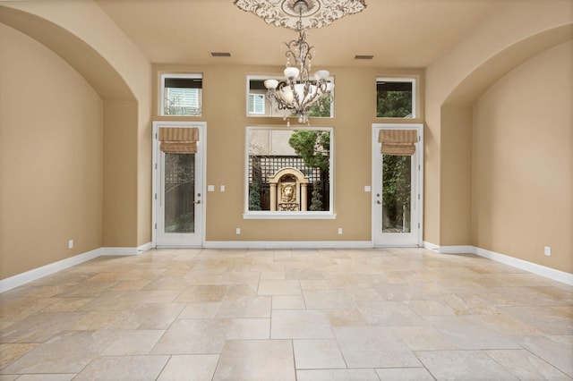 foyer featuring an inviting chandelier, baseboards, visible vents, and arched walkways