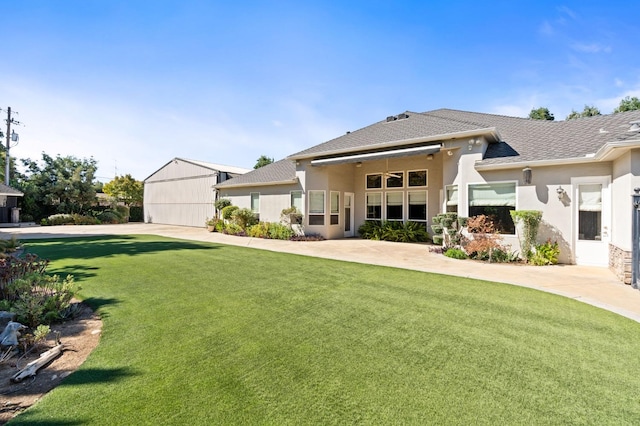 back of property featuring ceiling fan, roof with shingles, a lawn, and stucco siding