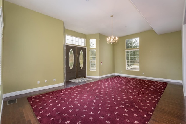 foyer entrance with plenty of natural light, a notable chandelier, and dark wood-type flooring