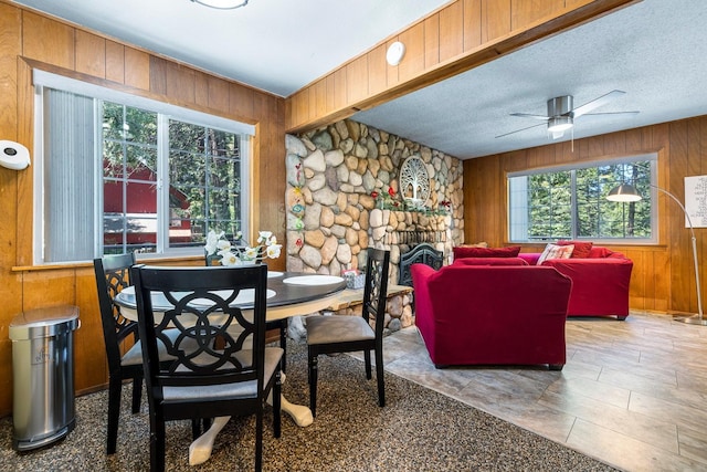 dining room featuring wood walls, ceiling fan, and a textured ceiling