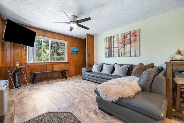 living room featuring wood walls, ceiling fan, and a textured ceiling