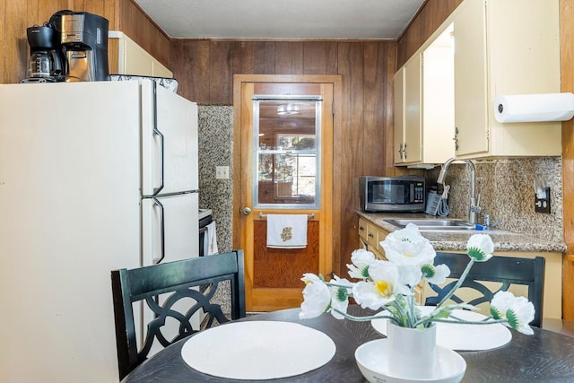 kitchen featuring wood walls, white fridge, sink, and backsplash