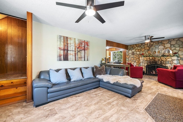 living room featuring a fireplace, ceiling fan, a textured ceiling, and wooden walls