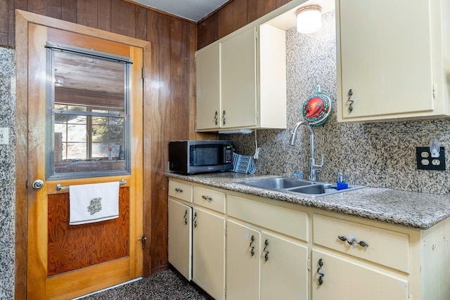 kitchen featuring tasteful backsplash, wooden walls, sink, and cream cabinetry