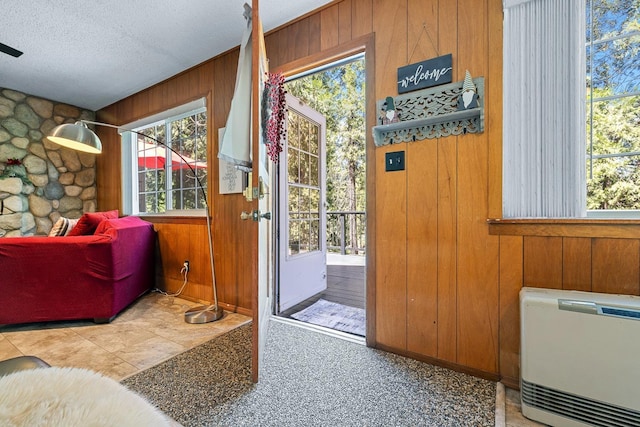 doorway to outside with a textured ceiling, heating unit, and wood walls