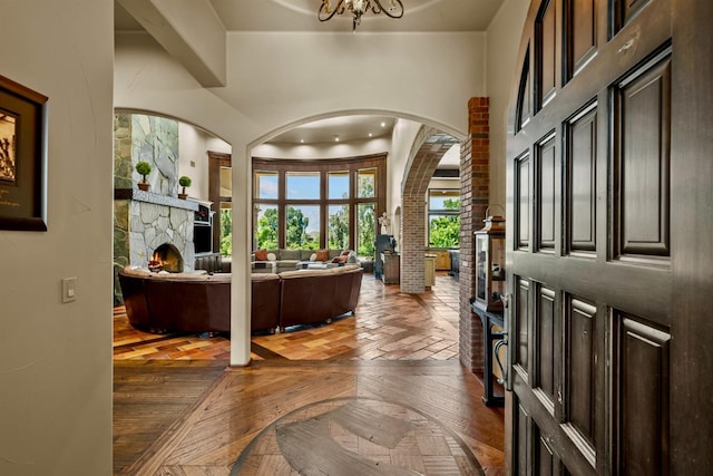 foyer entrance featuring an inviting chandelier, parquet flooring, and a stone fireplace