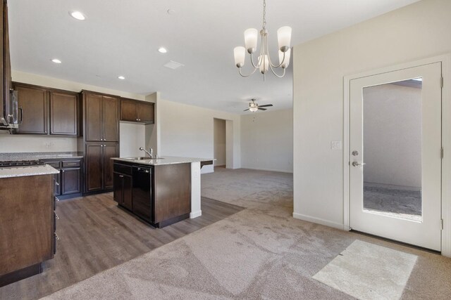 kitchen featuring decorative light fixtures, ceiling fan with notable chandelier, a center island with sink, dark brown cabinets, and wood-type flooring