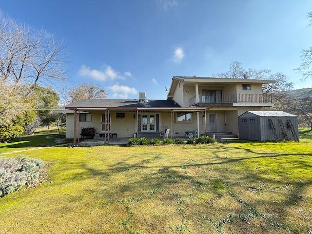 rear view of property featuring a shed, a lawn, a balcony, and central air condition unit