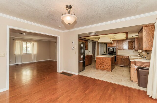 kitchen featuring stainless steel appliances, light hardwood / wood-style flooring, pendant lighting, a textured ceiling, and ornamental molding