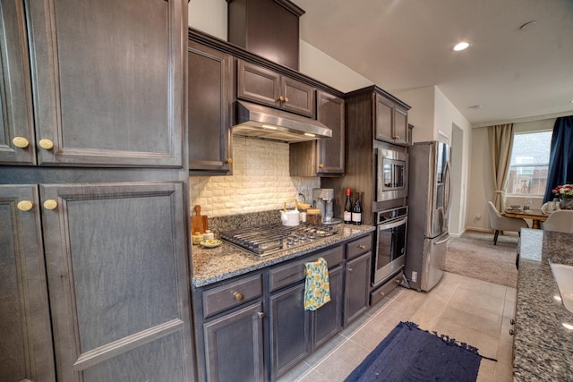 kitchen featuring backsplash, stone counters, dark brown cabinets, appliances with stainless steel finishes, and light tile floors