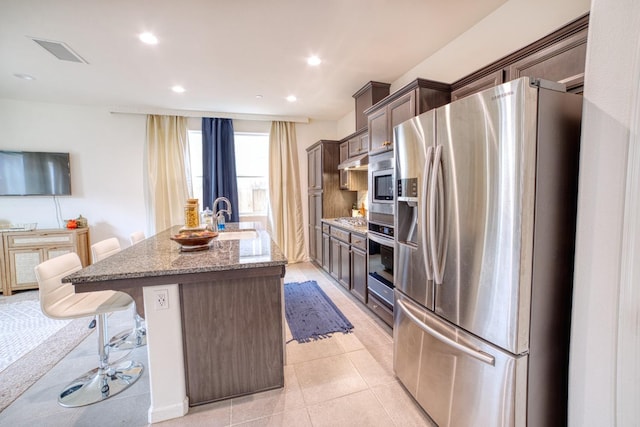 kitchen with stainless steel appliances, a center island with sink, a kitchen bar, light stone countertops, and sink