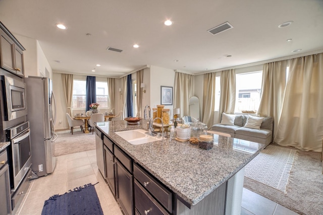 kitchen featuring stainless steel appliances, a kitchen island with sink, sink, and light tile floors