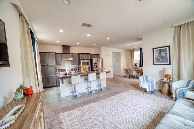 kitchen with light tile flooring, backsplash, stainless steel appliances, a center island with sink, and a kitchen bar