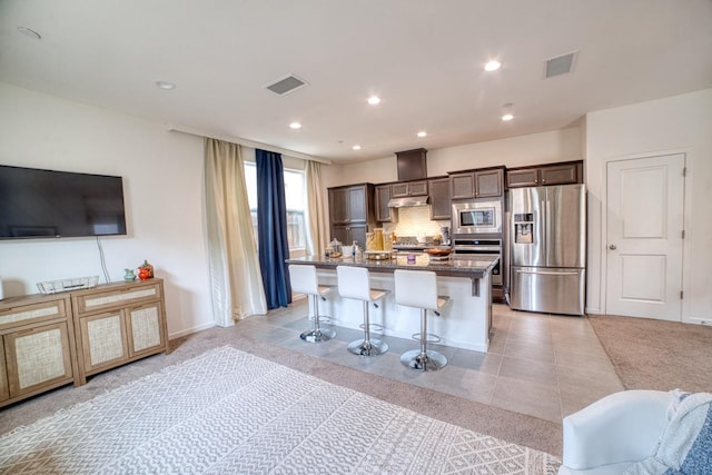 kitchen with dark stone counters, light tile flooring, a kitchen island, stainless steel appliances, and a breakfast bar area