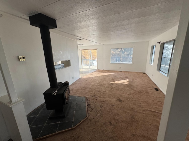 unfurnished living room with a textured ceiling, plenty of natural light, carpet, and a wood stove