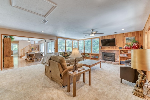 carpeted living room featuring wooden walls, a brick fireplace, and ceiling fan