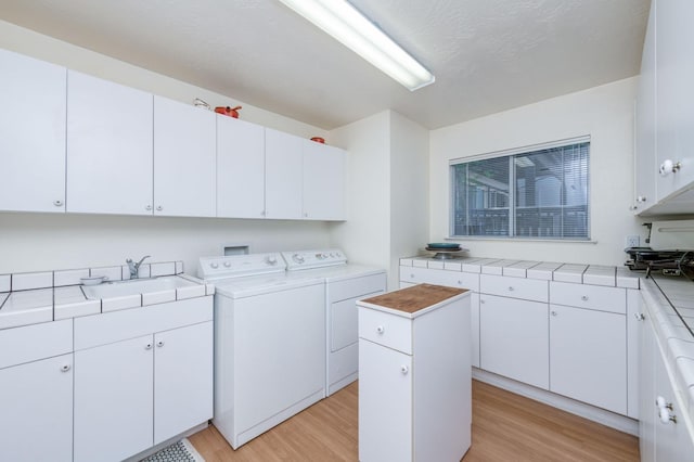 washroom featuring cabinets, sink, washing machine and clothes dryer, and light hardwood / wood-style flooring