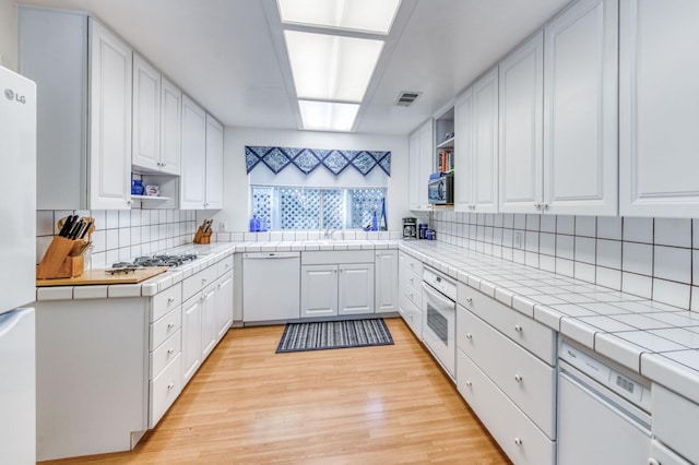 kitchen with stainless steel appliances, white cabinets, tile countertops, and light hardwood / wood-style flooring