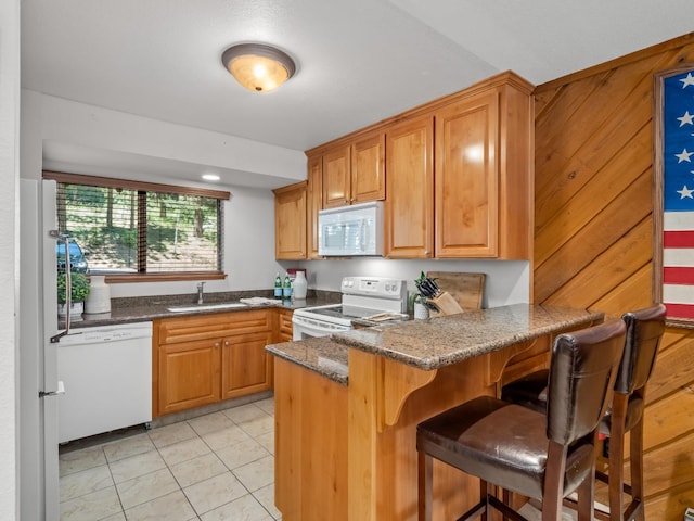 kitchen featuring white appliances, dark stone counters, a peninsula, light tile patterned flooring, and a sink