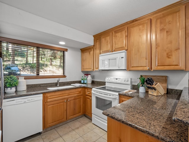 kitchen featuring light tile patterned floors, dark stone countertops, white appliances, and a sink