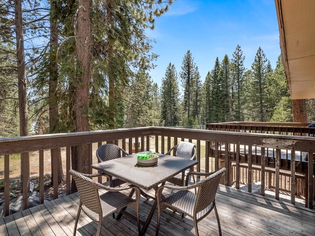 wooden terrace featuring a forest view and outdoor dining space