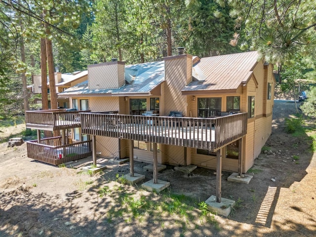 back of property with a wooden deck, a chimney, and metal roof